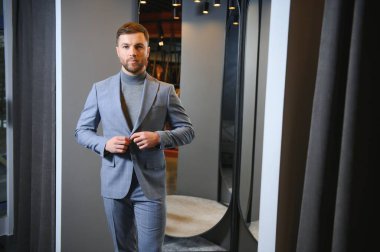 Erkek giyim mağazasında aynada takım elbise deneyen adam..