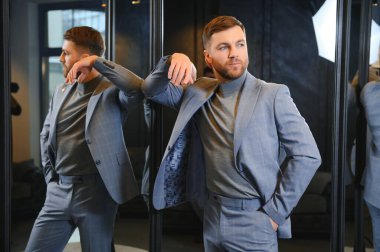 Erkek giyim mağazasında aynada takım elbise deneyen gülümseyen adam..