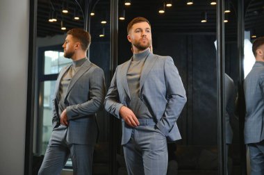 Modern genç yakışıklı işadamı kravat takım elbise dükkanda duran aynanın önünde ayarlama Klasik takım elbise giymiş.