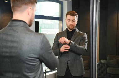 Modern genç yakışıklı işadamı kravat takım elbise dükkanda duran aynanın önünde ayarlama Klasik takım elbise giymiş.
