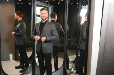 Modern genç yakışıklı işadamı kravat takım elbise dükkanda duran aynanın önünde ayarlama Klasik takım elbise giymiş.