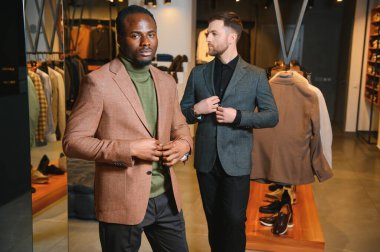 Klasik takım elbiseli iki şık, çok kültürlü adam bir giyim mağazasında duruyor..