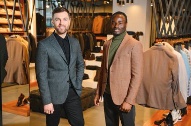 Klasik takım elbiseli iki şık, çok kültürlü adam bir giyim mağazasında duruyor..