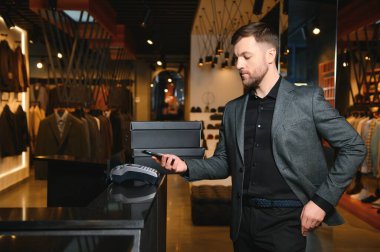 Yeni kıyafetler ve ayakkabılarla dolu kutular taşıyan ve telefonla ödeme yapan mutlu müşteriler..