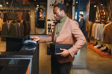 Kutular dolusu yeni kıyafet ve ayakkabı taşıyan ve kredi kartıyla ödeme yapan mutlu müşteriler..