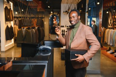 Kutular dolusu yeni kıyafet ve ayakkabı taşıyan ve kredi kartıyla ödeme yapan mutlu müşteriler..