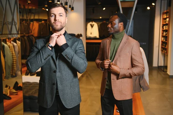 Klasik takım elbiseli iki şık, çok kültürlü adam bir giyim mağazasında duruyor..