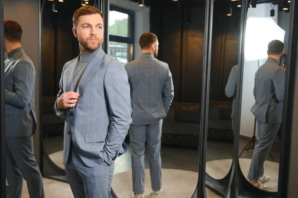 Modern genç yakışıklı işadamı kravat takım elbise dükkanda duran aynanın önünde ayarlama Klasik takım elbise giymiş.