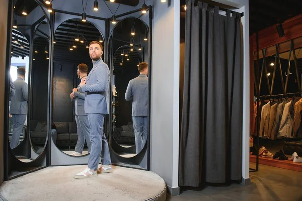 Modern genç yakışıklı işadamı kravat takım elbise dükkanda duran aynanın önünde ayarlama Klasik takım elbise giymiş.