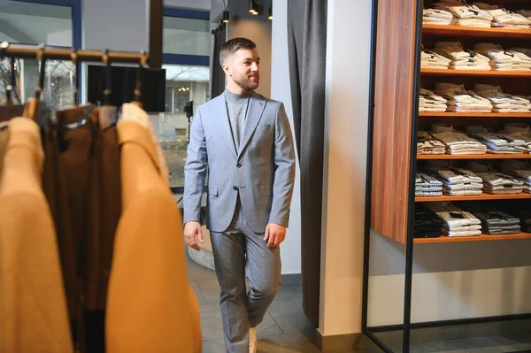 sale, shopping, fashion, style and people concept - elegant young man in suit in mall or clothing store.