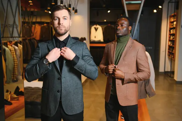 İş stili. Erkek modası. Zarif klasik takım elbiseli ve gözlüklü iki saygıdeğer adam şık erkek giyim mağazasında yan yana durur..