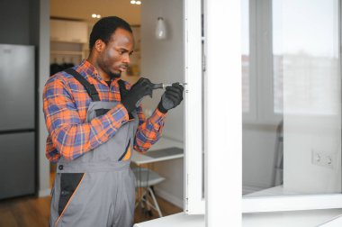 Evdeki oturma odasına plastik pencereler monte eden ya da ayarlayan işçi.