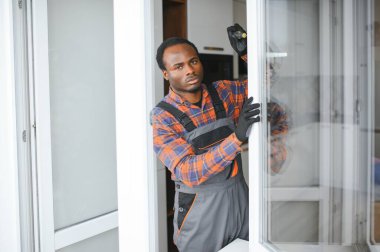 Evdeki oturma odasına plastik pencereler monte eden ya da ayarlayan işçi.