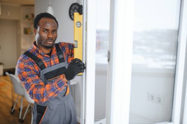 Evdeki oturma odasına plastik pencereler monte eden ya da ayarlayan işçi.