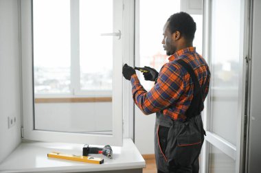 Evdeki oturma odasına plastik pencereler monte eden ya da ayarlayan işçi.