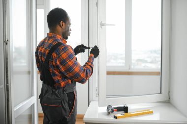 Evdeki oturma odasına plastik pencereler monte eden ya da ayarlayan işçi.