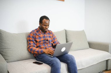 Çevrimiçi bir dünyayla bağlantı kurmak. Evde dinlenirken dizüstü bilgisayar kullanan mutlu bir gencin fotoğrafı..