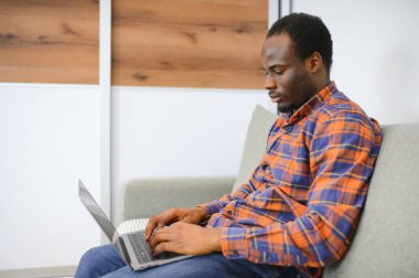 Çevrimiçi bir dünyayla bağlantı kurmak. Evde dinlenirken dizüstü bilgisayar kullanan mutlu bir gencin fotoğrafı..