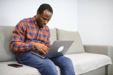Çevrimiçi bir dünyayla bağlantı kurmak. Evde dinlenirken dizüstü bilgisayar kullanan mutlu bir gencin fotoğrafı..
