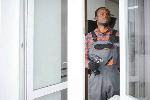 a african repairman repairs, adjusts or installs metal-plastic windows in the apartment.