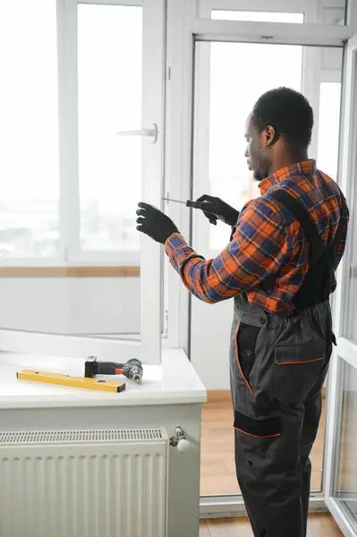 a african repairman repairs, adjusts or installs metal-plastic windows in the apartment.