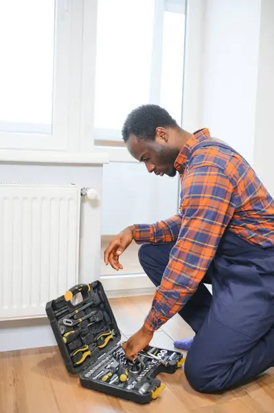 Repair heating radiator close-up. African man repairing radiator with wrench. Removing air from the radiator.