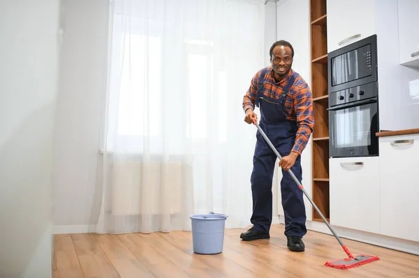 Young african man washes the floor with a mop in the room.