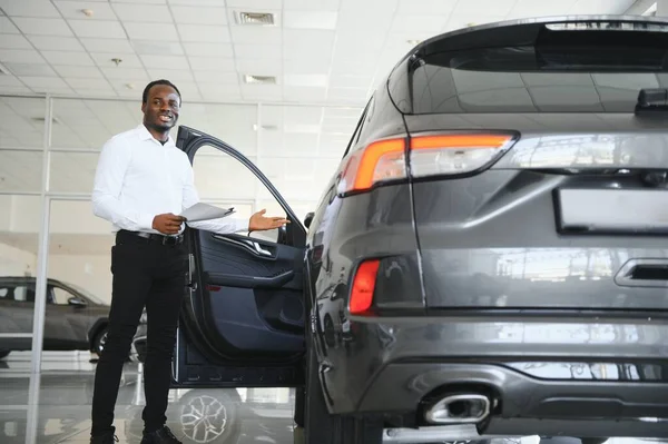 Genç Afro-Amerikan araba galerisi müdürü araç galerisinde duruyor..
