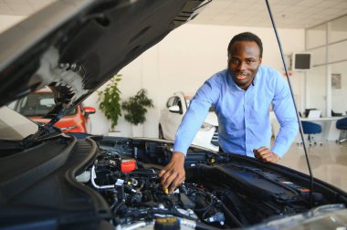Yakışıklı Afrikalı işadamı satın almadan önce bir arabayı inceliyor, tüm özelliklerini ve özelliklerini kontrol ediyor..