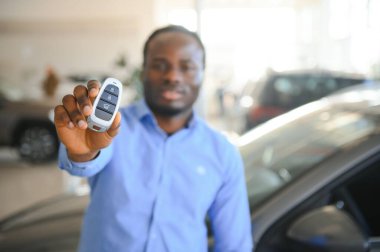 Gülümseyen adam arabanın anahtarlarını tutuyor ve arka planda yeni bir araba sunuyor..