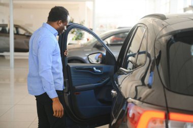 Hayalindeki araba. Mutlu genç Afrikalı adam galeride bir araba seçerken heyecanlı görünüyor..