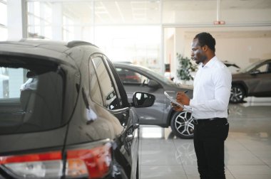 Genç Afro-Amerikan araba galerisi müdürü araç galerisinde duruyor..