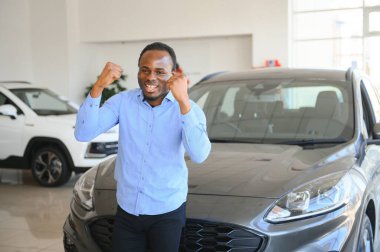 Hayalindeki araba. Mutlu genç Afrikalı adam galeride bir araba seçerken heyecanlı görünüyor..