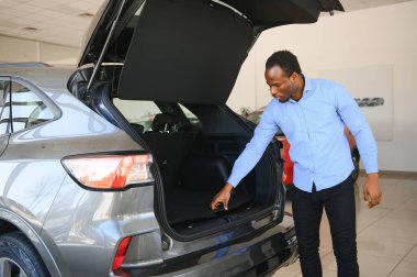 Hayalindeki araba. Mutlu genç Afrikalı adam galeride bir araba seçerken heyecanlı görünüyor..