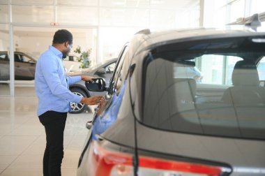 Hayalindeki araba. Mutlu genç Afrikalı adam galeride bir araba seçerken heyecanlı görünüyor..