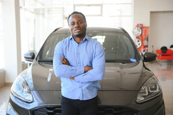 Hayalindeki araba. Mutlu genç Afrikalı adam galeride bir araba seçerken heyecanlı görünüyor..