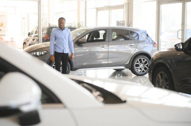 Hayalindeki araba. Mutlu genç Afrikalı adam galeride bir araba seçerken heyecanlı görünüyor..