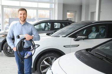 Sakallı adam yeni şarj kablosu deniyor. Araba galerisinde şarj istasyonu var. Elektrikli araba alma kavramı. Zeki ekolojik yaşam.