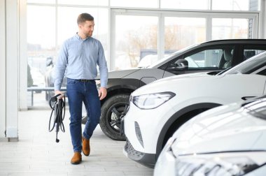 Elektrikli araba alma kavramı. Yakışıklı iş adamı galeride elektrikli arabanın yanında duruyor..