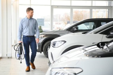 Mutlu bir adam bir araba galerisinde yeni bir elektrikli araba seçer. Ekolojik araba alma kavramı.