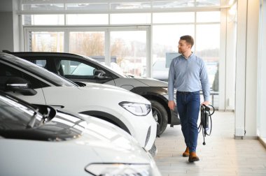 Sakallı adam yeni şarj kablosu deniyor. Araba galerisinde şarj istasyonu var. Elektrikli araba alma kavramı. Zeki ekolojik yaşam.