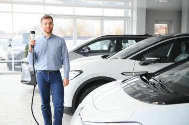 Sakallı adam yeni şarj kablosu deniyor. Araba galerisinde şarj istasyonu var. Elektrikli araba alma kavramı. Zeki ekolojik yaşam.