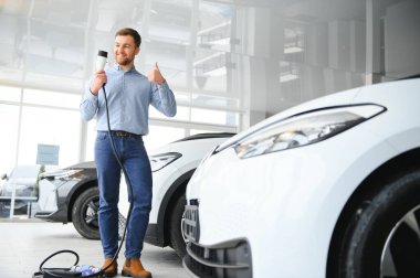 Elektrikli araba alma kavramı. Yakışıklı iş adamı galeride elektrikli arabanın yanında duruyor..