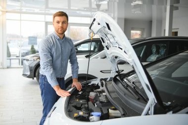 Mutlu bir adam bir araba galerisinde yeni bir elektrikli araba seçer. Ekolojik araba alma kavramı.