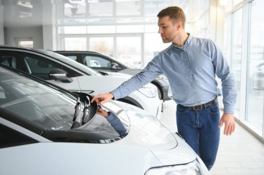 Mutlu bir adam bir araba galerisinde yeni bir elektrikli araba seçer. Ekolojik araba alma kavramı.
