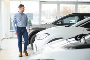 Elektrikli araba alma kavramı. Yakışıklı iş adamı galeride elektrikli arabanın yanında duruyor..
