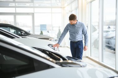 Mutlu bir adam bir araba galerisinde yeni bir elektrikli araba seçer. Ekolojik araba alma kavramı.