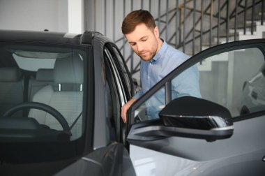 Genç bir adam araba galerisinde yeni bir araba seçiyor.