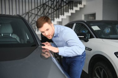 Mutlu bir adam bir araba galerisinde yeni bir elektrikli araba seçer. Ekolojik araba alma kavramı.