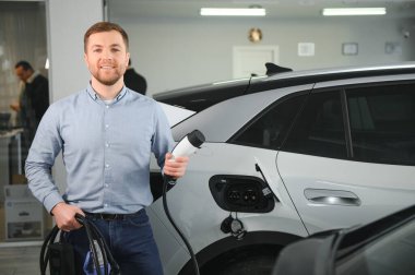Elektrikli araba alma kavramı. Yakışıklı iş adamı galeride elektrikli arabanın yanında duruyor..